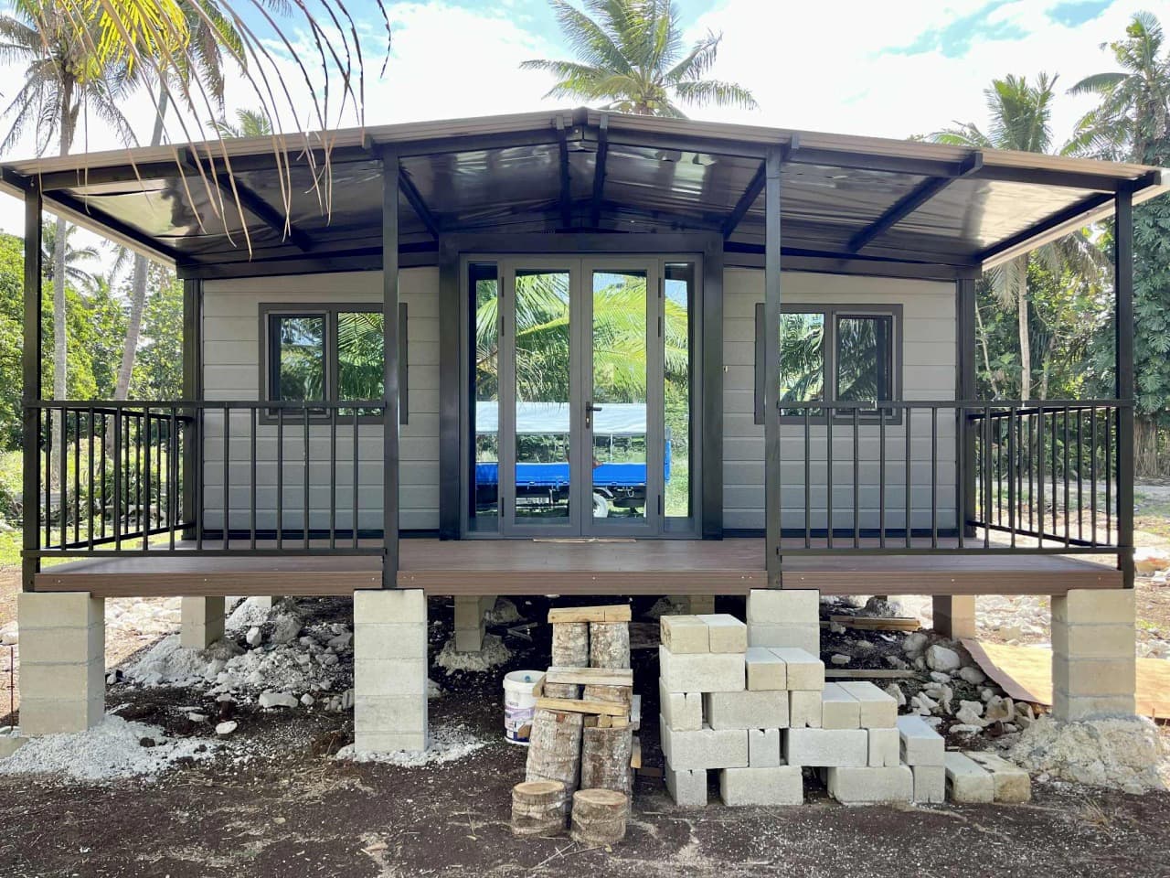 Delivered gray expandable home with a covered porch among palm trees.