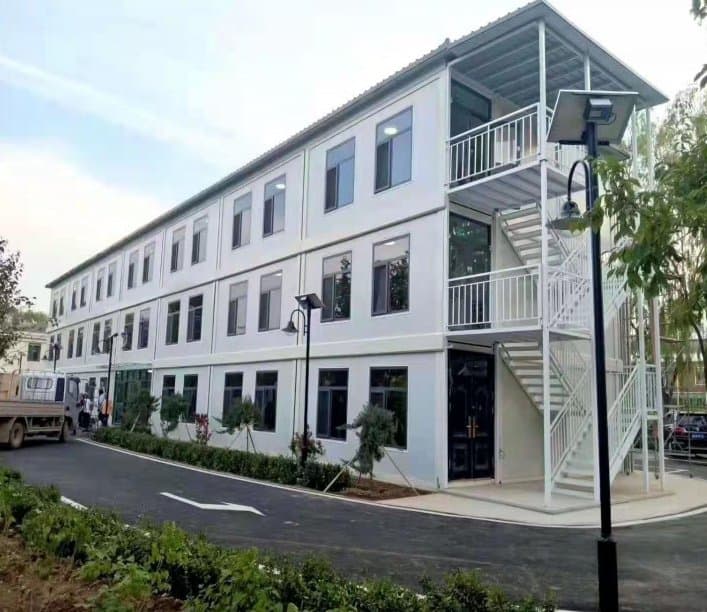 Three-story white modular apartment building with balconies and exterior stairs.