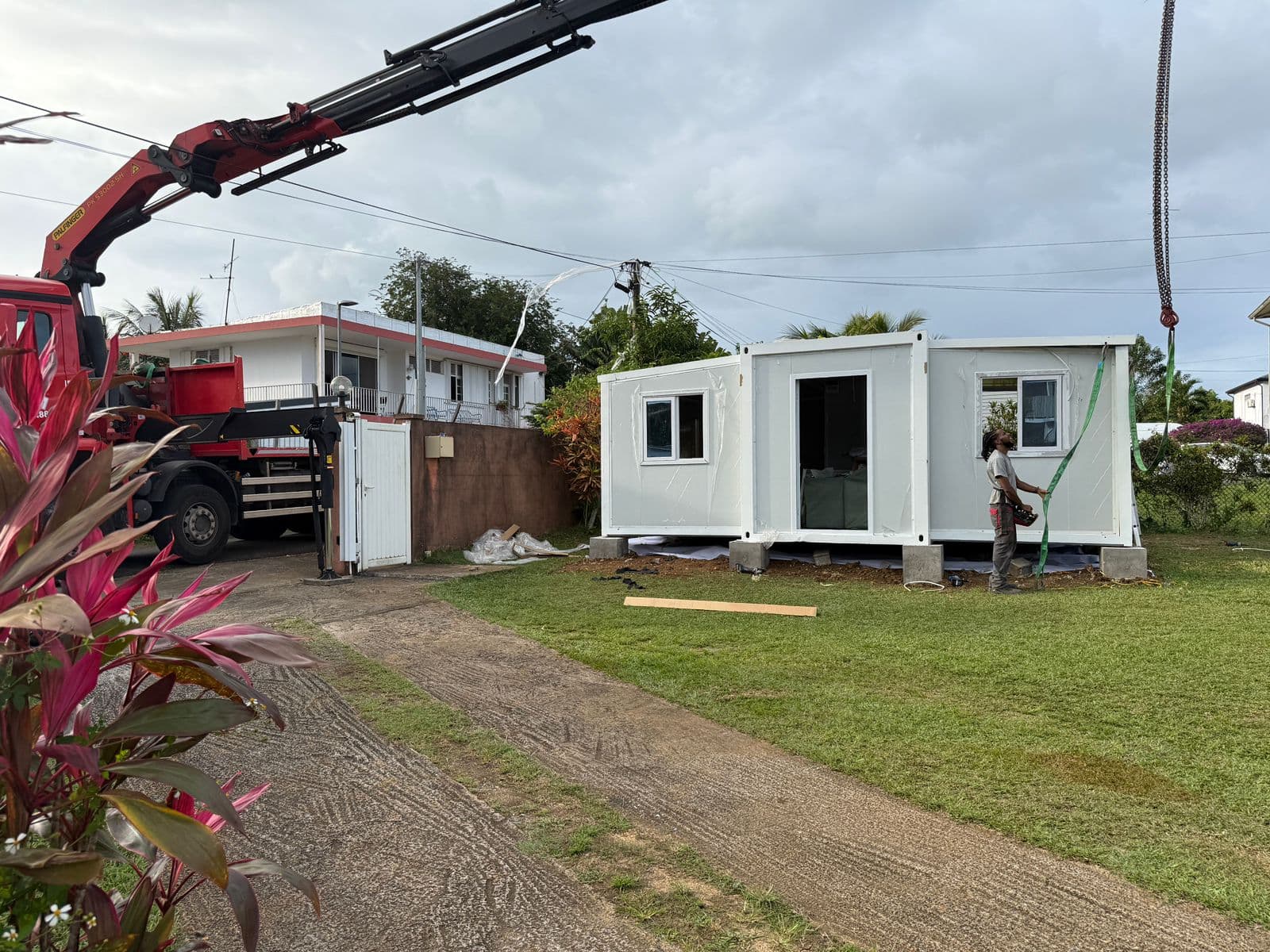 A white expandable home being delivered by crane truck.
